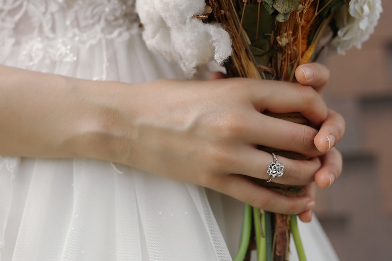 a bride holding her bouquet and wearing an emerald cut halo engagement ring