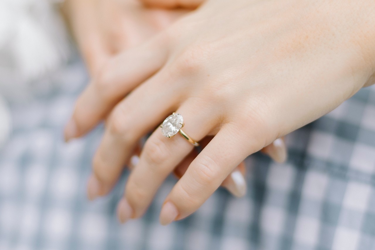 a pair of crossed hands, one of which is adorned with an oval cut solitaire engagement ring