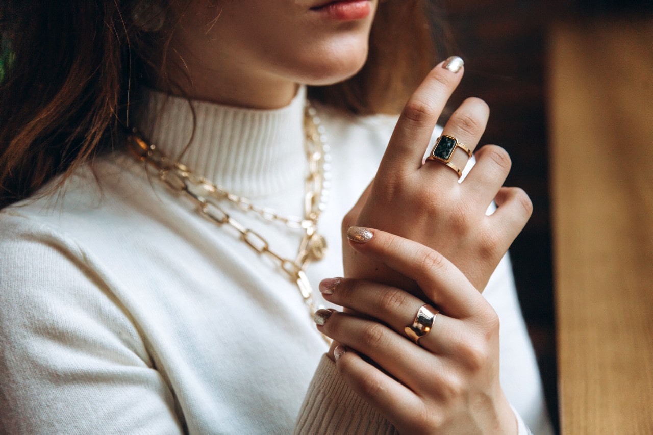 Close-up of a woman wearing a white turtleneck sweater accessorized with layered gold chains and rings.