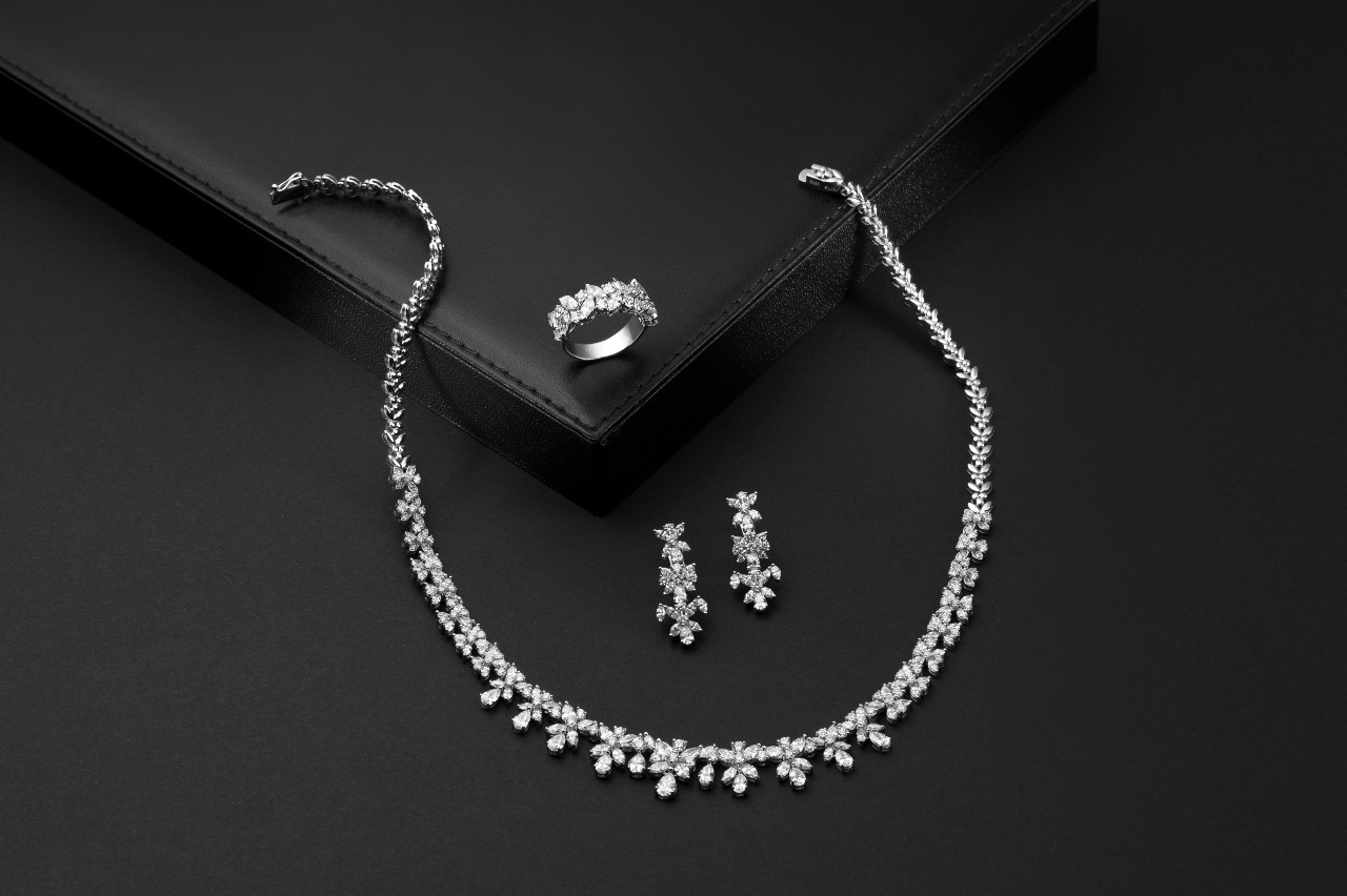 An elegant jewelry set, featuring a sparkling diamond necklace, matching earrings, and a ring on a black background.