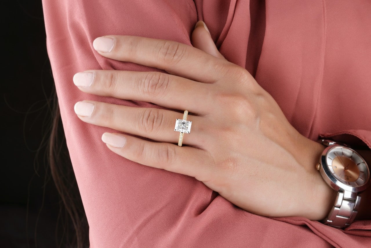 A close-up of a woman’s hand with a radiant-cut diamond engagement ring on top of her pink long-sleeve.