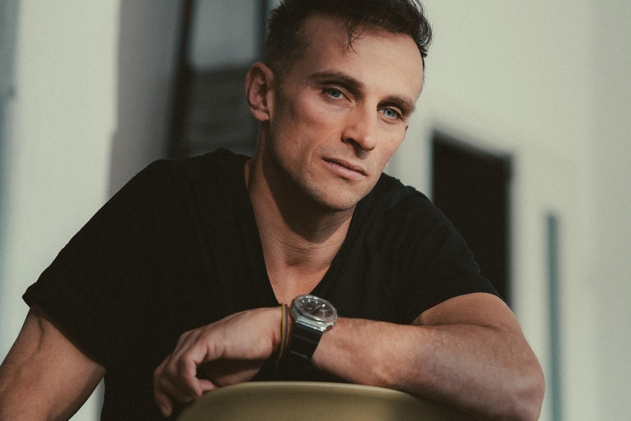 A man sitting backward in a chair and wearing a stainless steel watch with a black band.