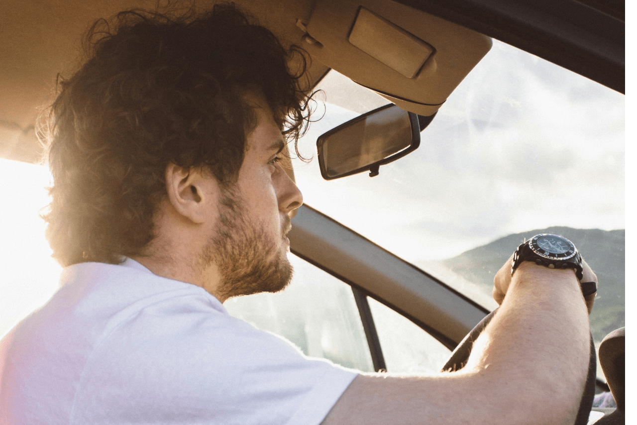 A man driving and resting his arm on the steering wheel wearing a black watch.