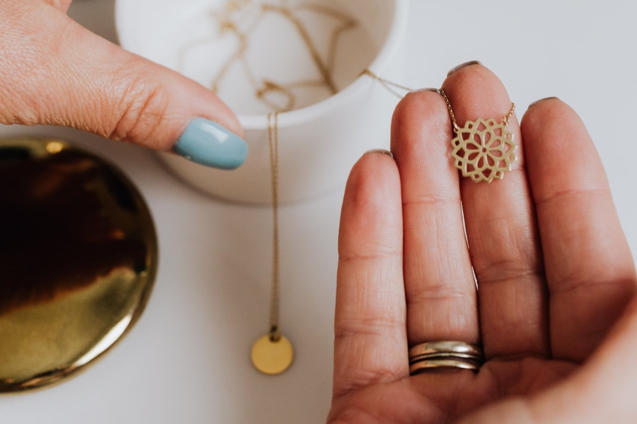 a person’s hand holding a small yellow gold floral necklace