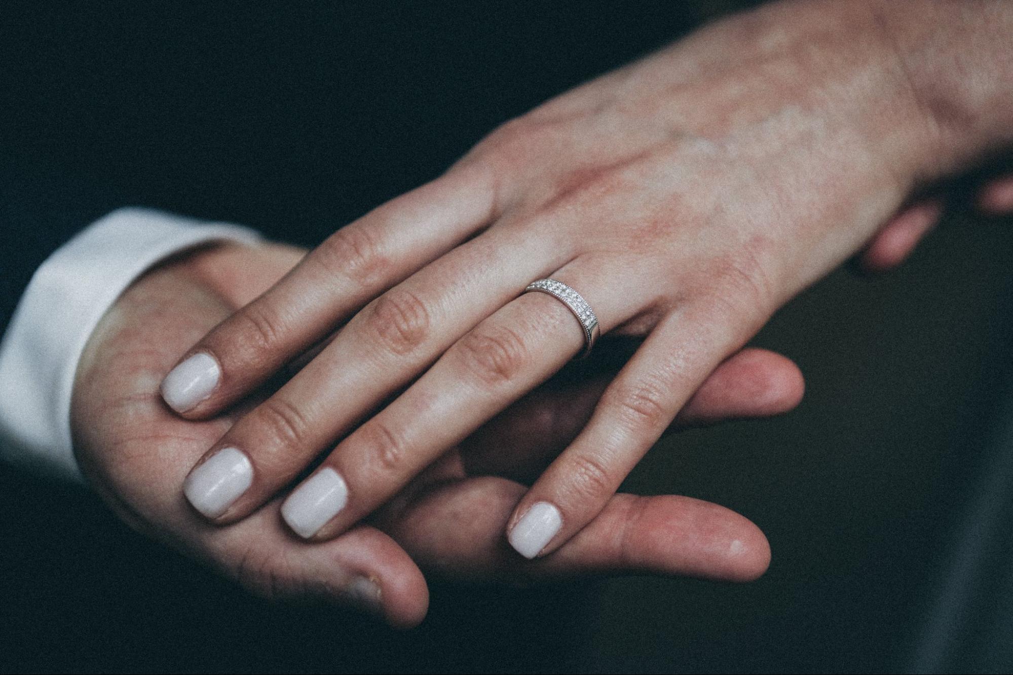 A bride resting her hand on her groom’s hand. She has a pavé diamond white gold wedding band.