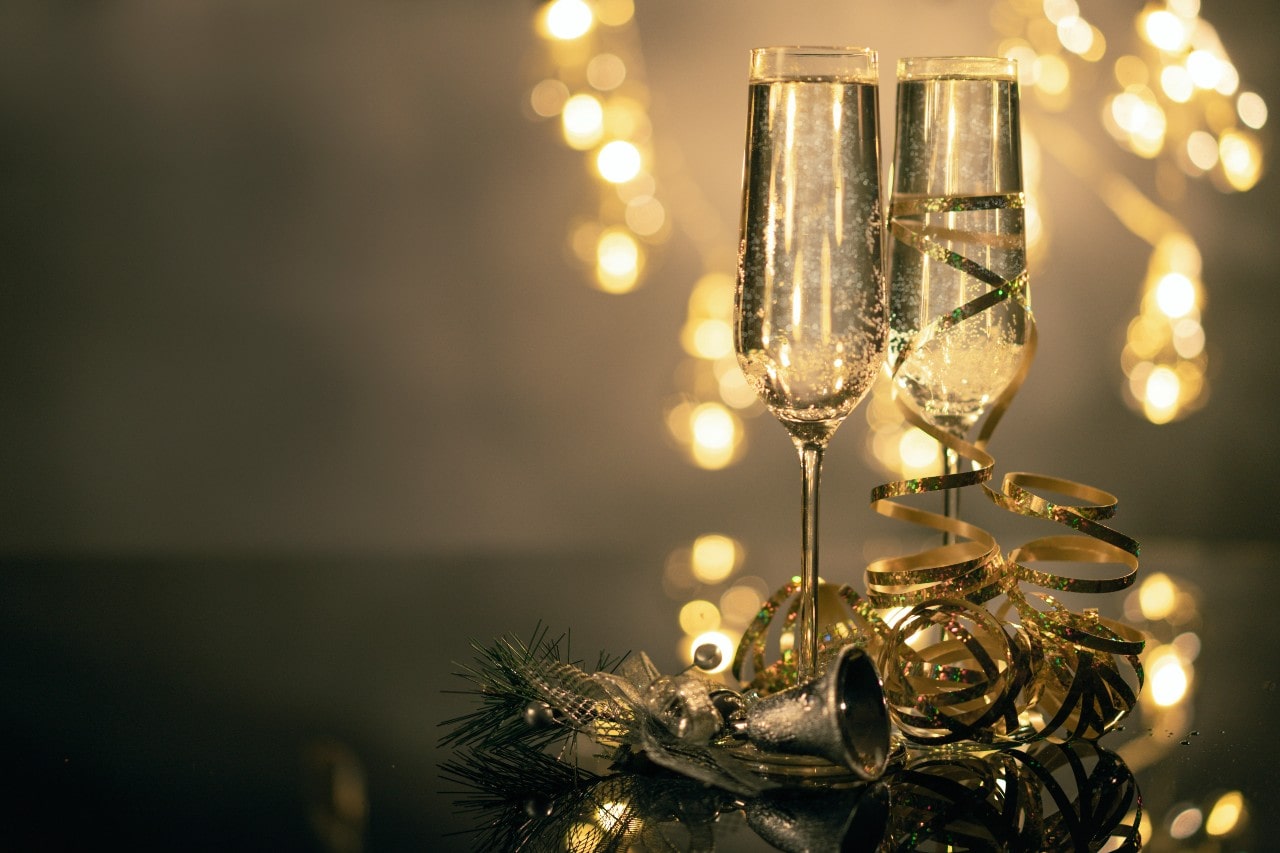 A duo of champagne flutes on a table with gold ribbon and NYE decorations.