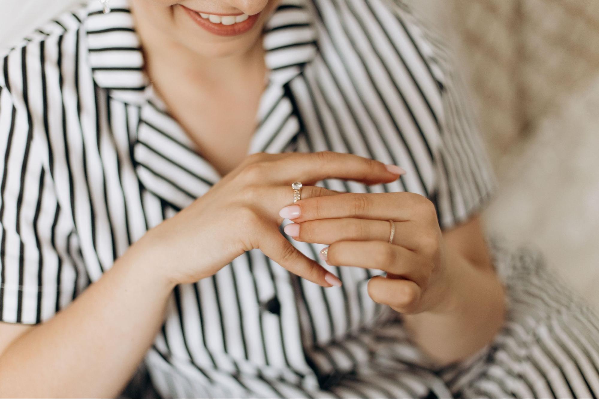 A smiling woman in a striped shirt tries on a glistening diamond ring.