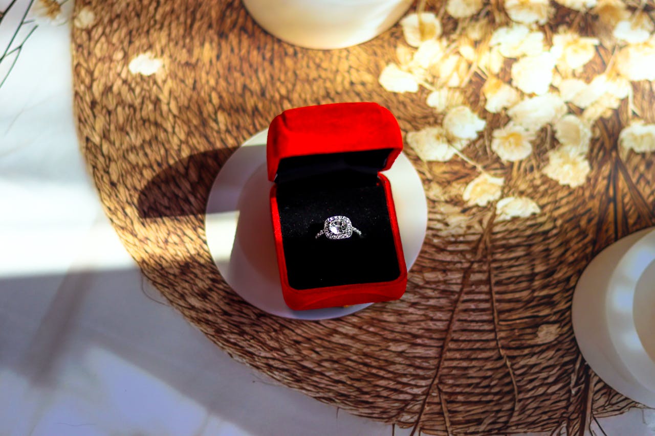 Close-up of a white gold halo engagement ring in a red and black velvet box on top of the wooden tupperware