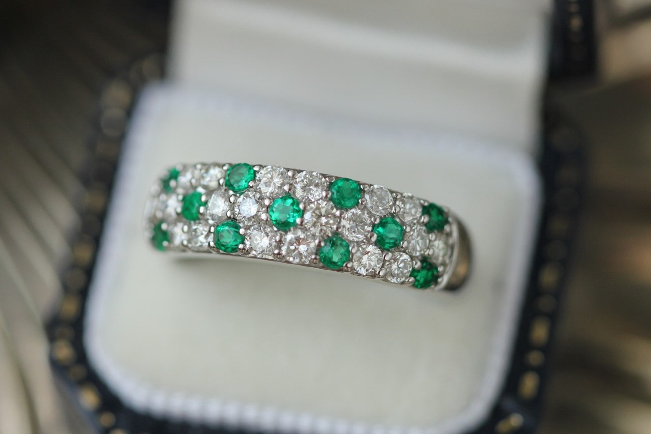 a white gold band featuring pave set emeralds and diamonds in a ring box