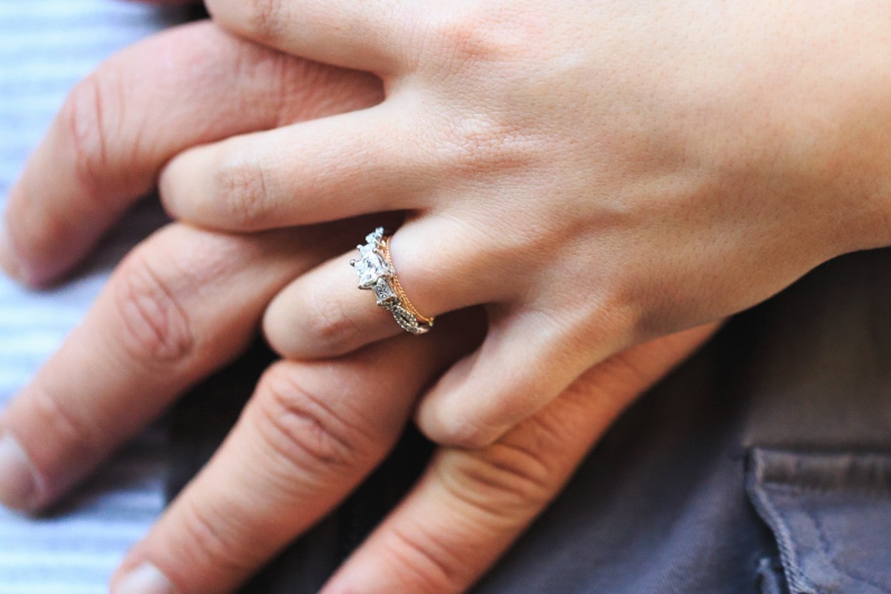 a couple’s hands intertwined, the woman wearing a mixed metal engagement ring
