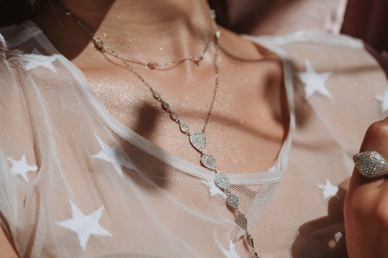 close up image of a woman’s neckline, adorned with two white gold diamond necklaces