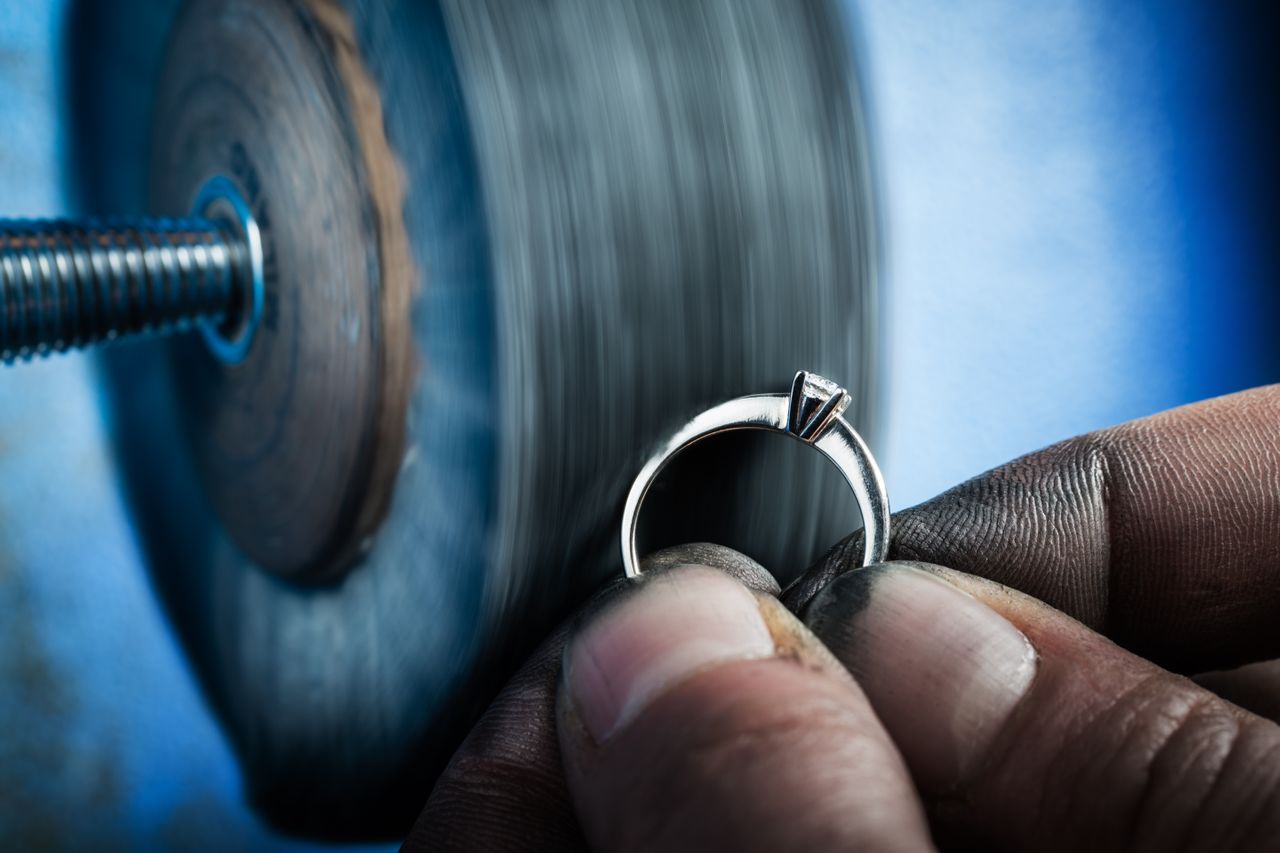 A jeweler polishes a white gold solitaire engagement ring setting using a rotary tool.