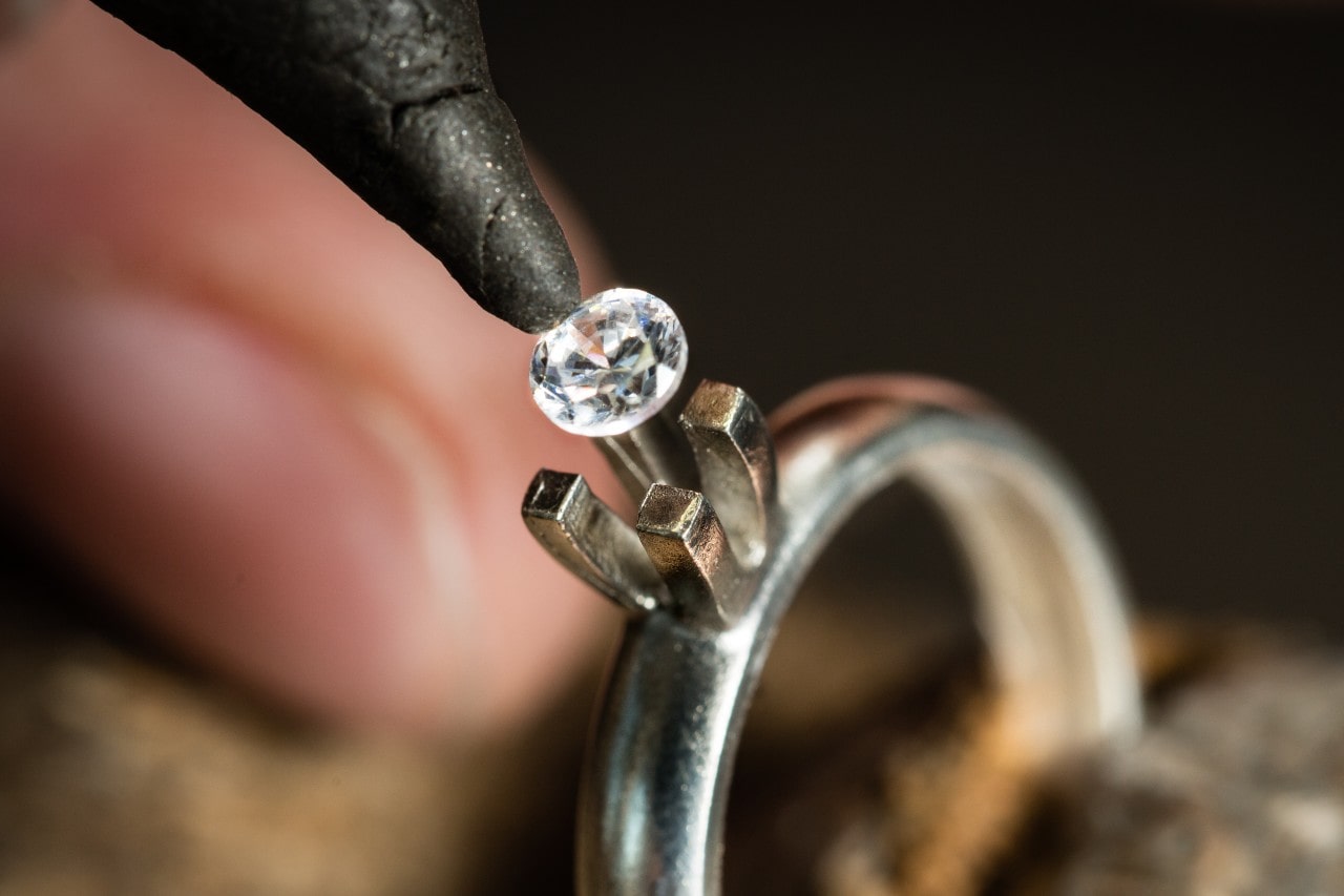 A jeweler sets a sparkling gemstone into a silver ring setting.