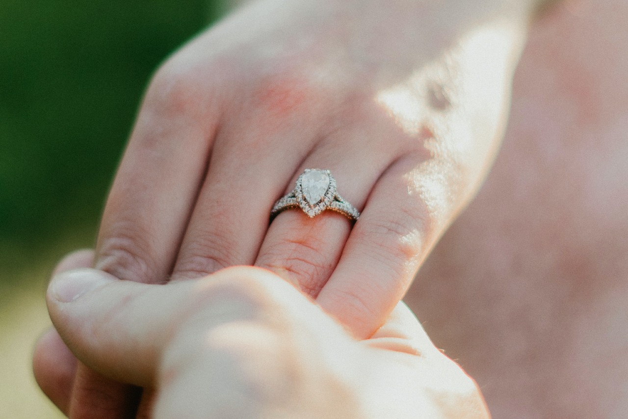 a man holding a woman’s hand, who is wearing a pear shape engagement ring