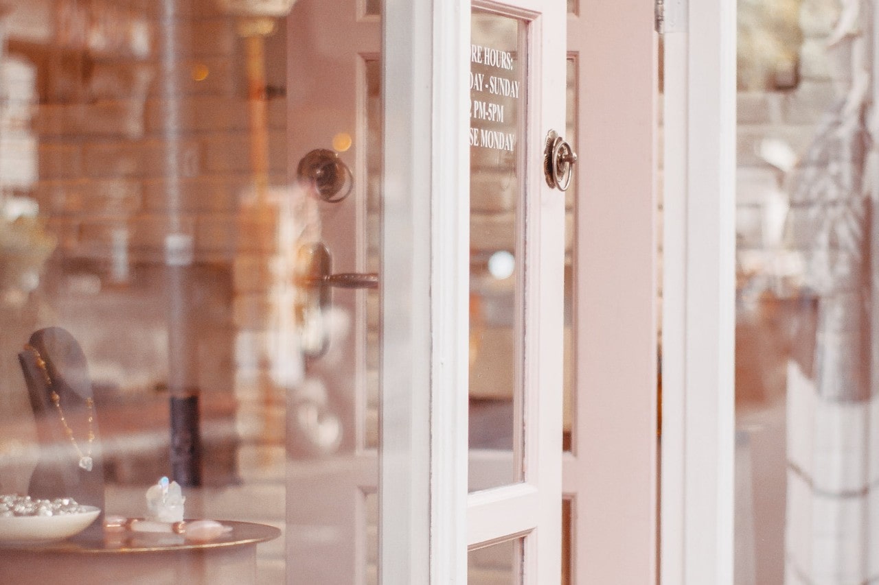 Chic jewelry boutique with a partially open soft pink door revealing a necklace elegantly showcased on a display bust inside.