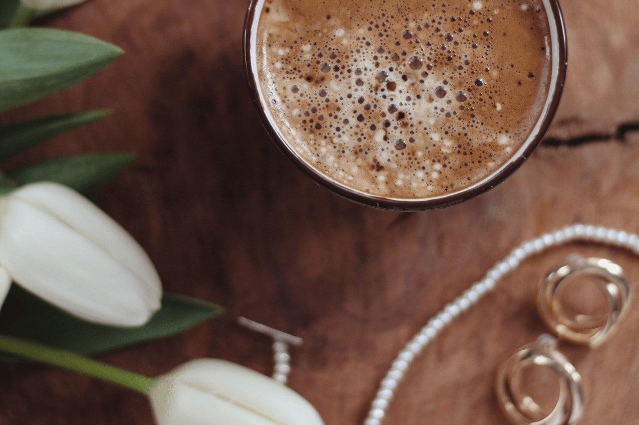 a cup of hot cocoa next to pieces of fashion jewelry