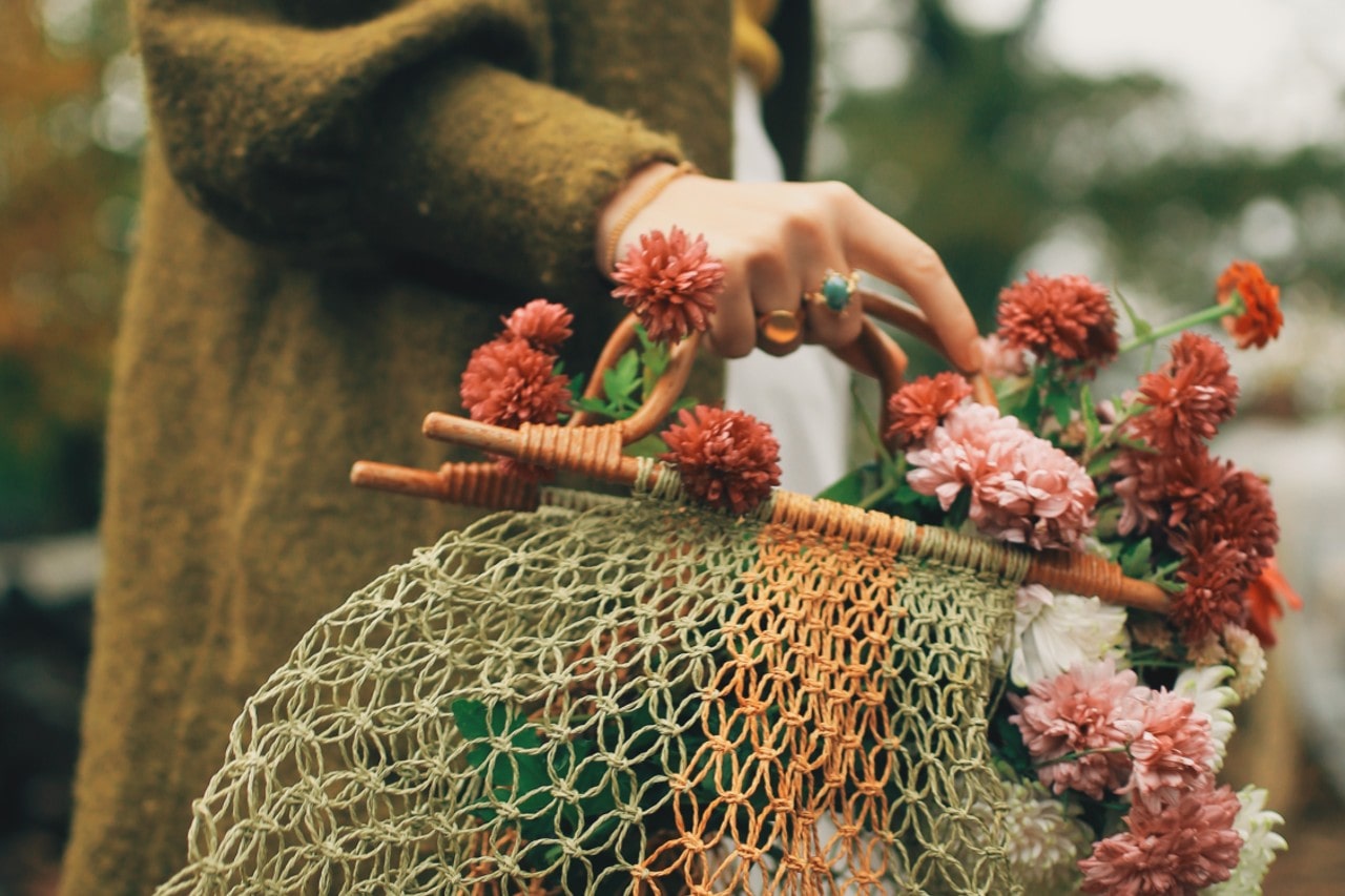 A woman in a cardigan and gemstone fashion rings holds a basket with seasonal wildflowers.