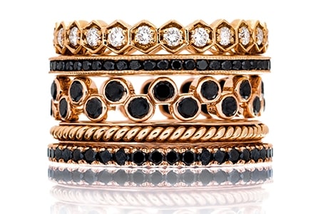 A stack of rose gold fashion rings with diamonds and black diamonds.
