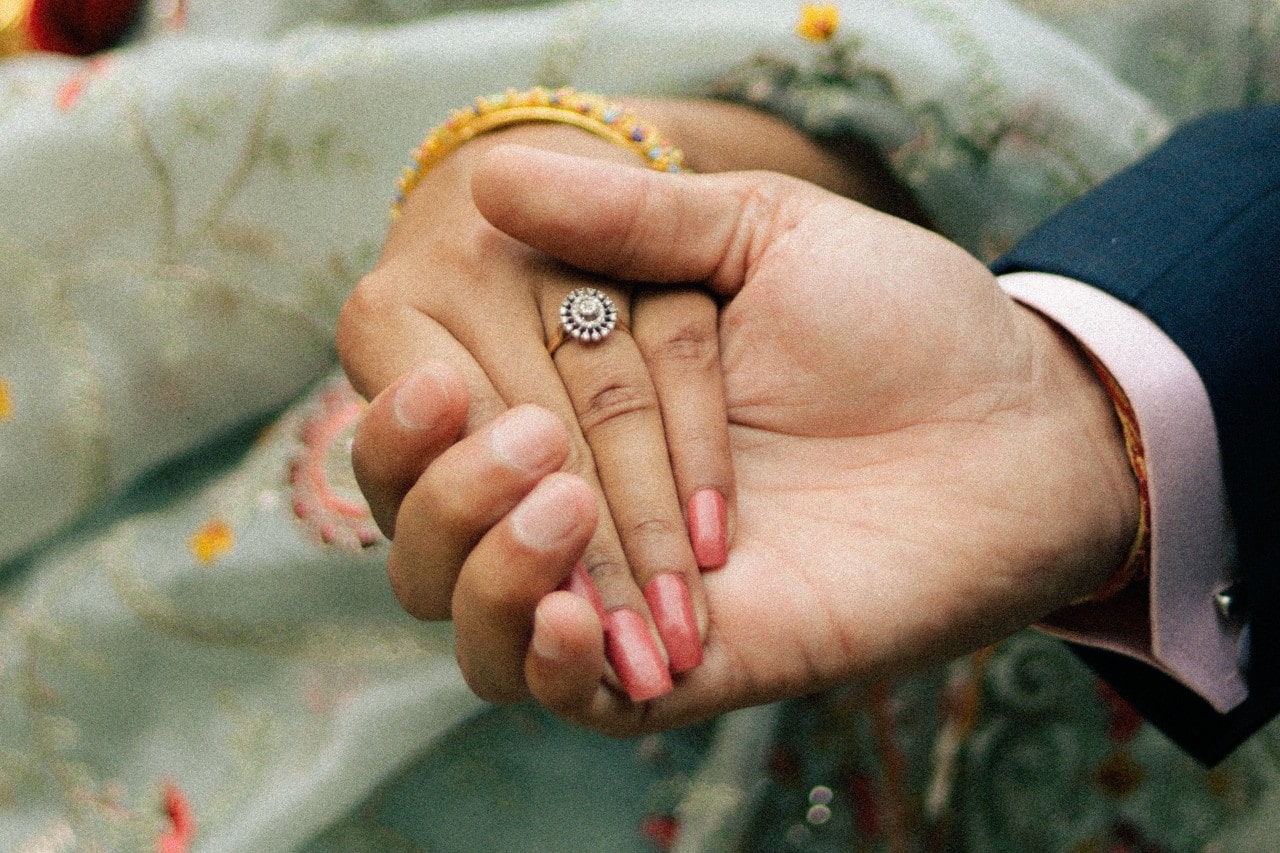 a man holding a woman’s hand who is wearing a rose gold halo set engagement ring