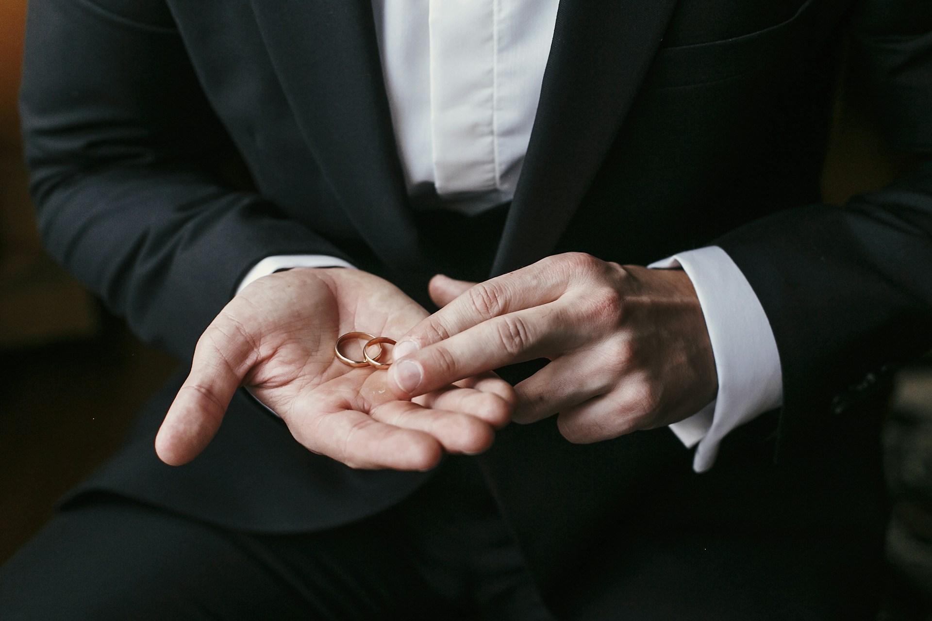 a groom holding two matching yellow gold wedding bands