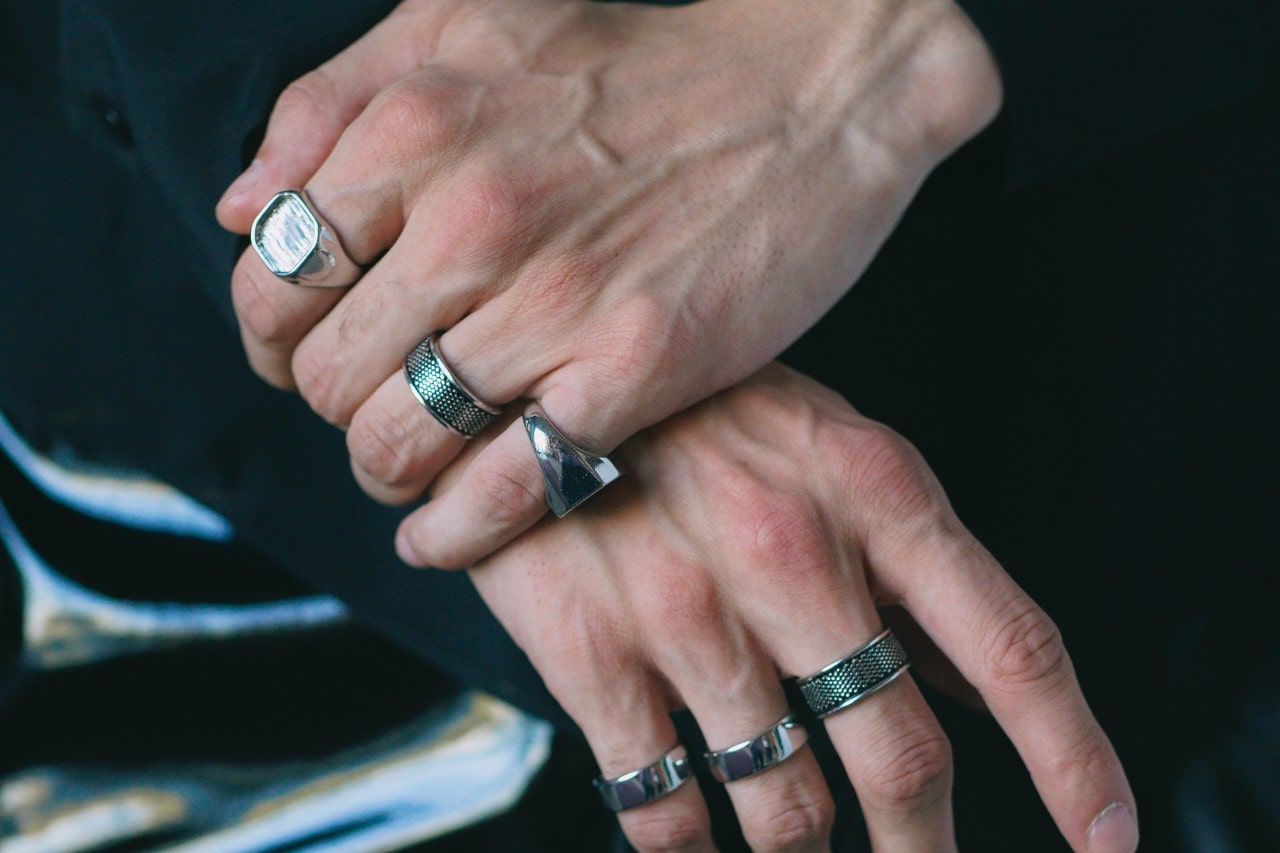 a man’s hands crossed over one another, donning thick silver rings