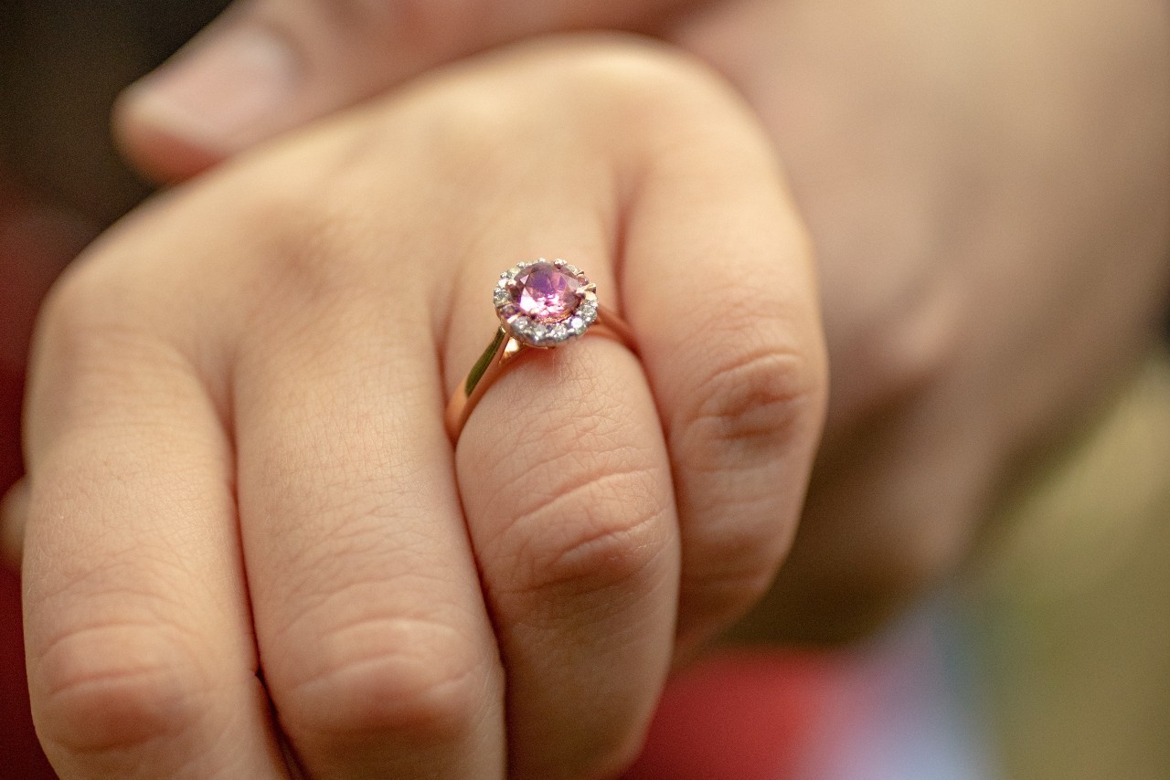 close up image of a woman’s hand wearing a rose gold engagement ring with a purple stone