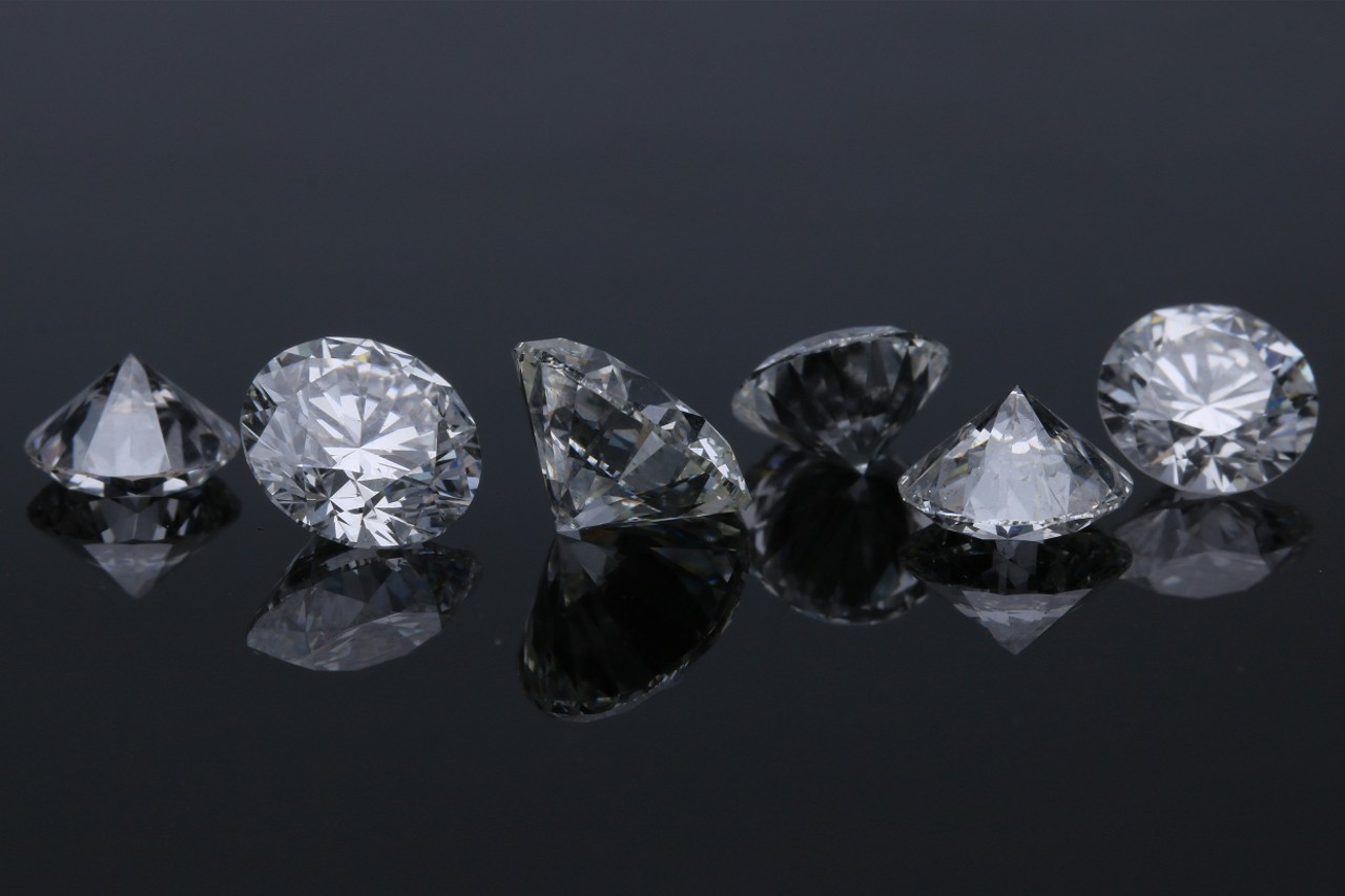 A row of loose round-cut diamonds displayed on a glossy black surface