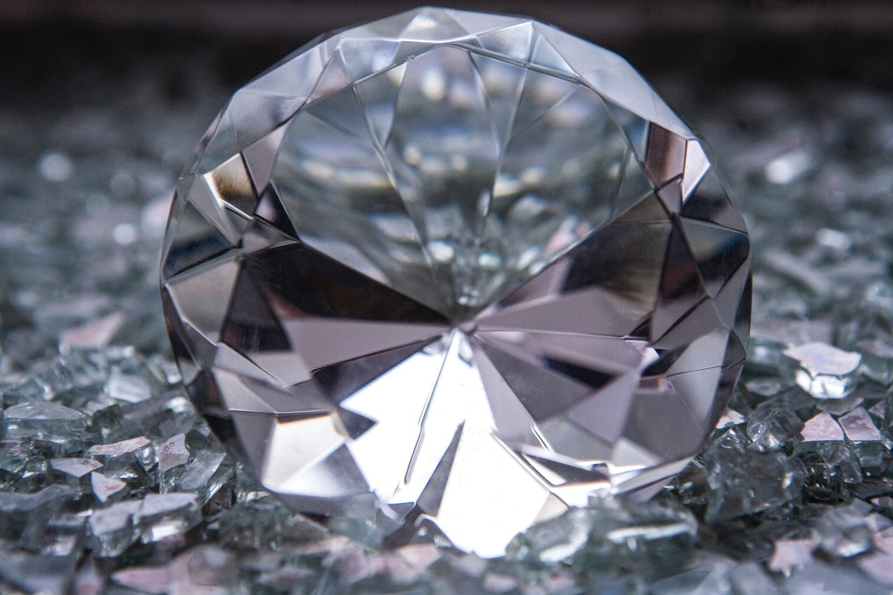 Close-up of a large, round-cut diamond resting on scattered shards of glass.