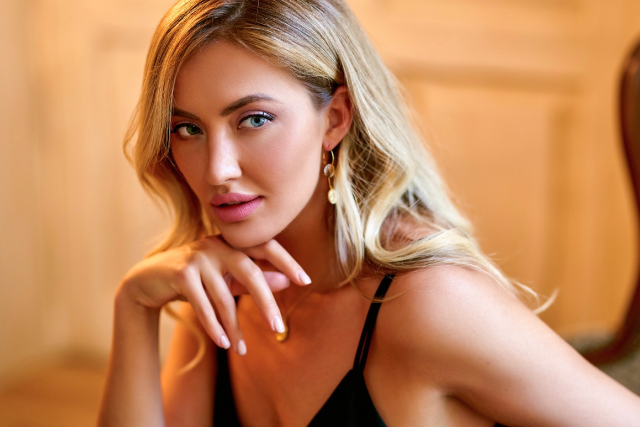 A woman with blond hair gazing at the side, showcasing drop yellow gold earrings.