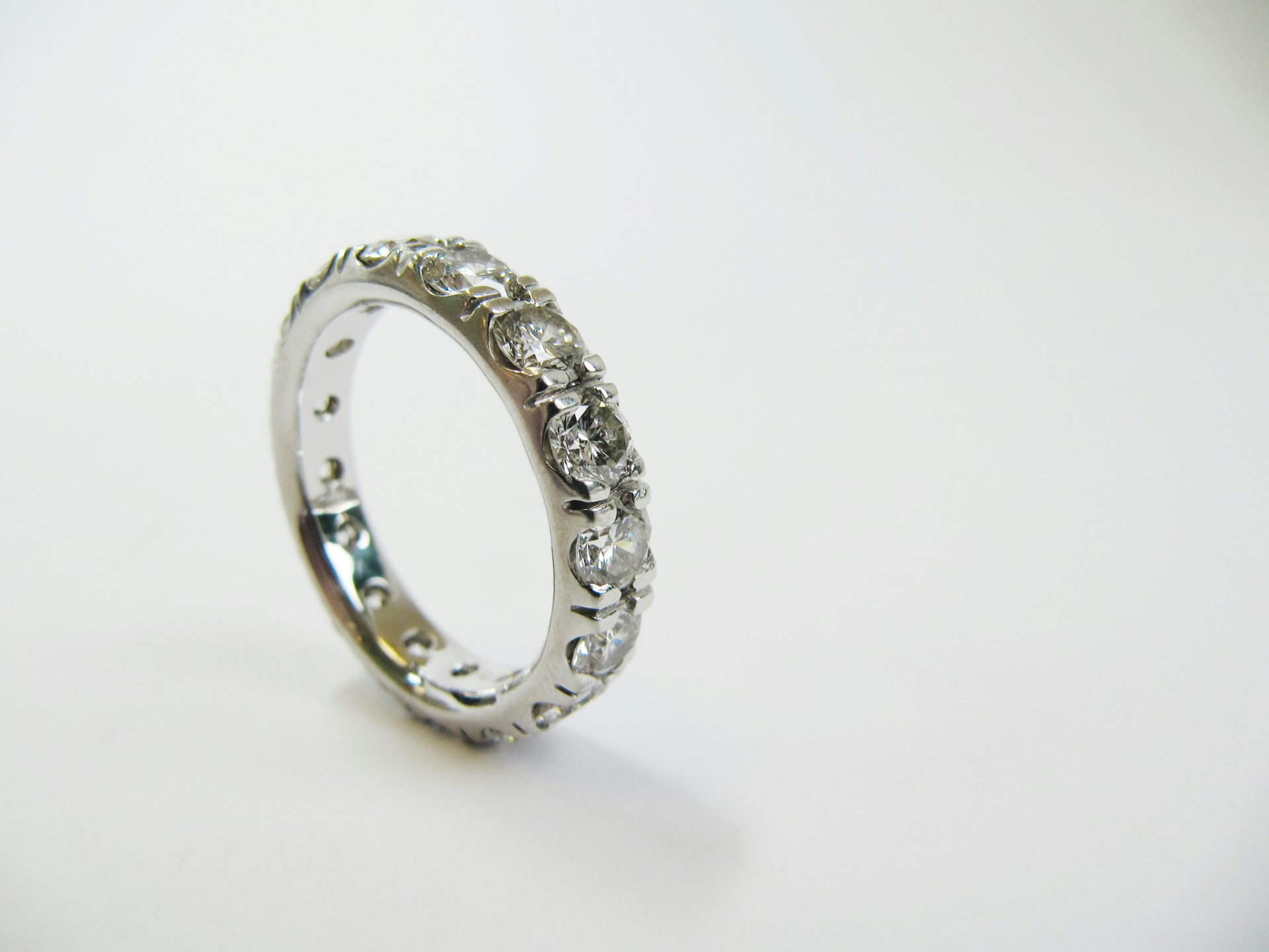 a white gold, prong set wedding band featuring round cut diamonds against a white background