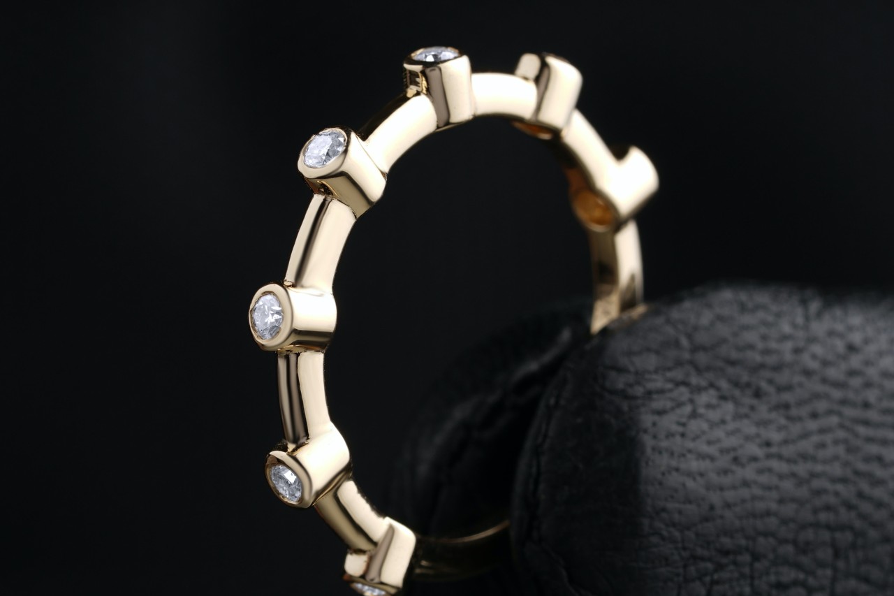 a yellow gold wedding band featuring bezel set diamonds held by gloved fingers