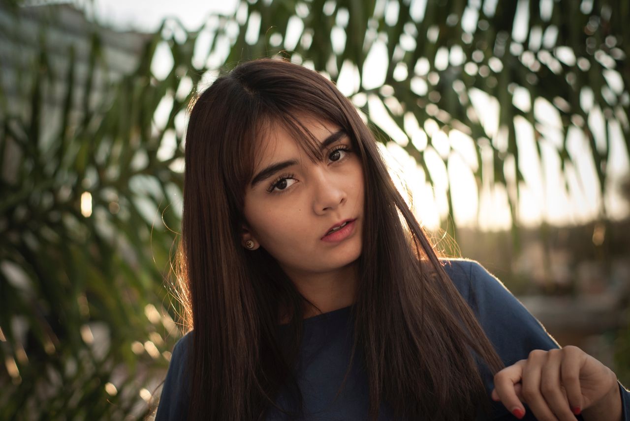 A girl with brown hair stands against a sun, showcasing yellow gold stud earrings