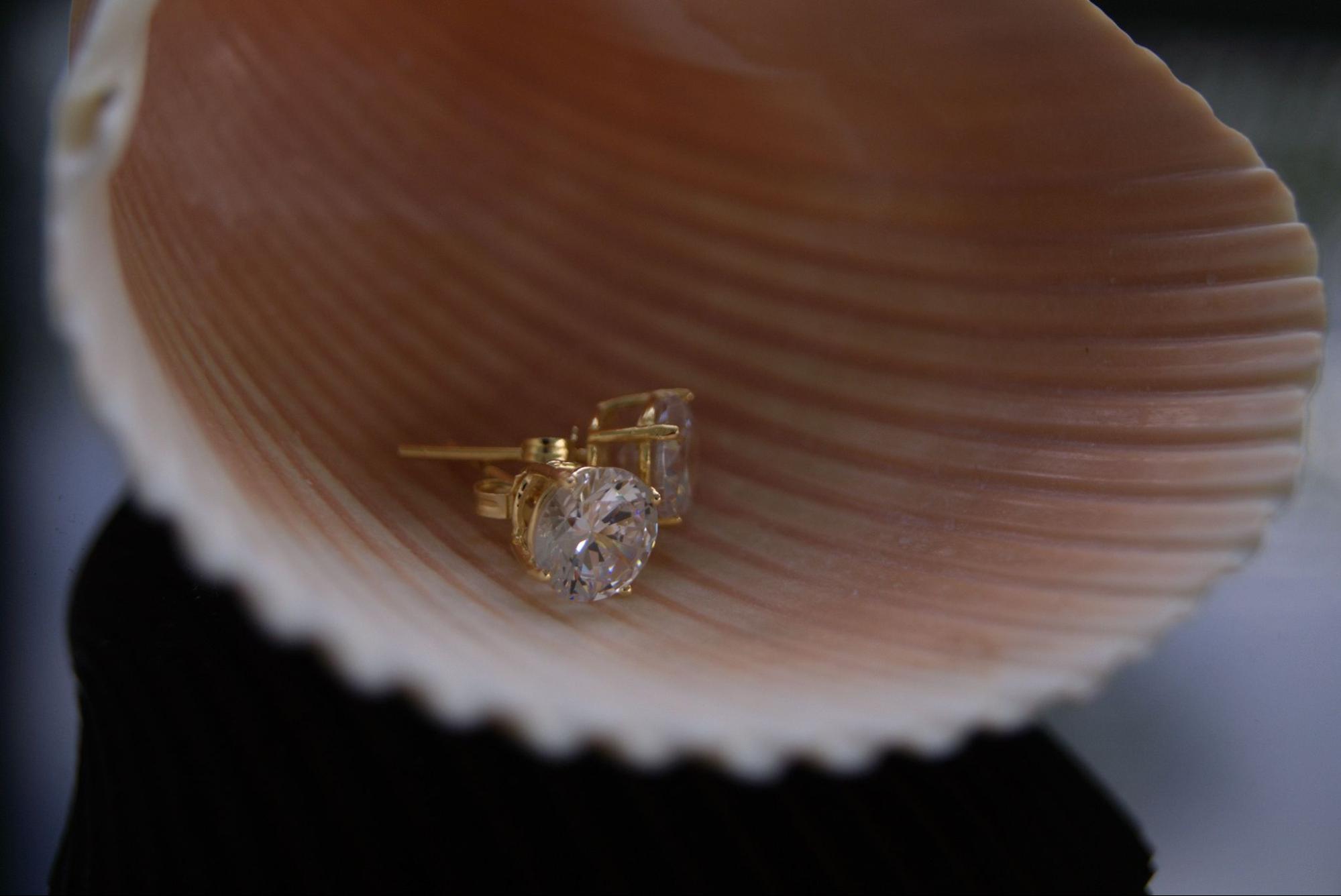 A close up of yellow gold diamond stud earrings lying on the big shell