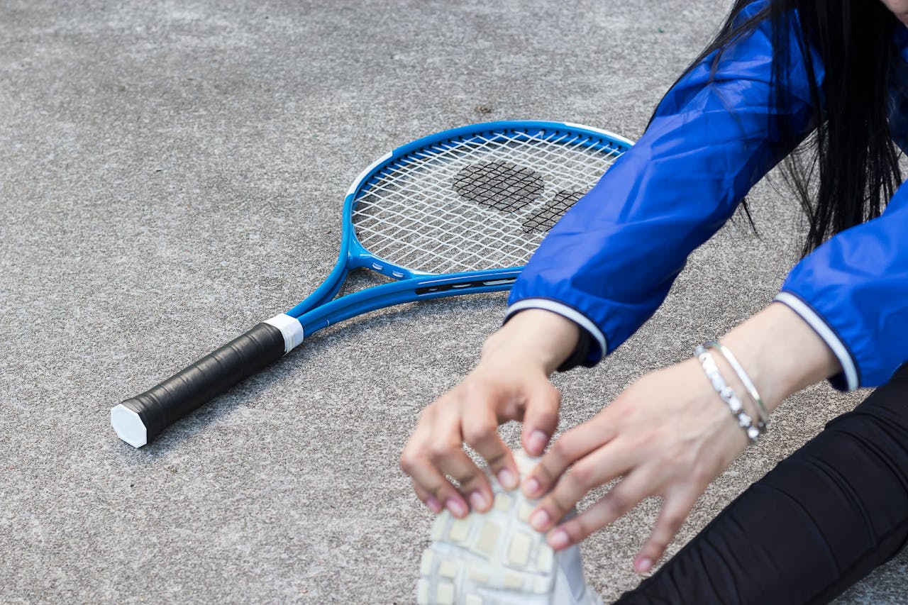 A wide view of a tennis player stretching, with two bracelets visible on her wrist.