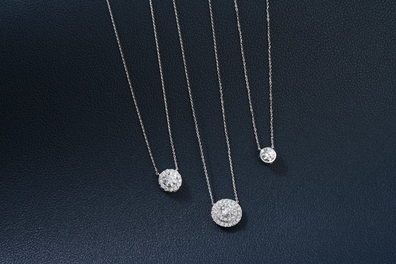 A close-up of three diamond pendant necklaces on a black leather backdrop.