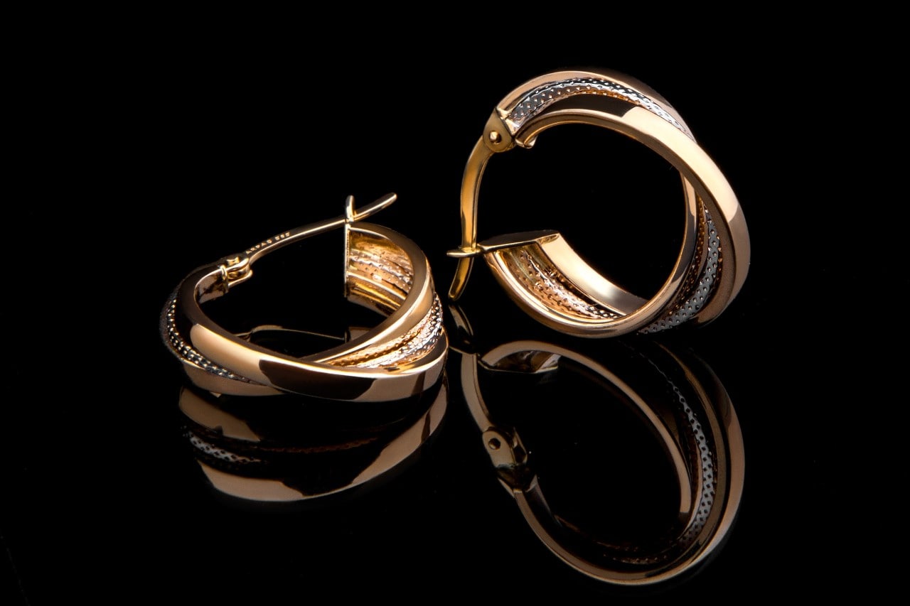 A close-up of a stunning pair of two-tone gold earrings on a black backdrop.