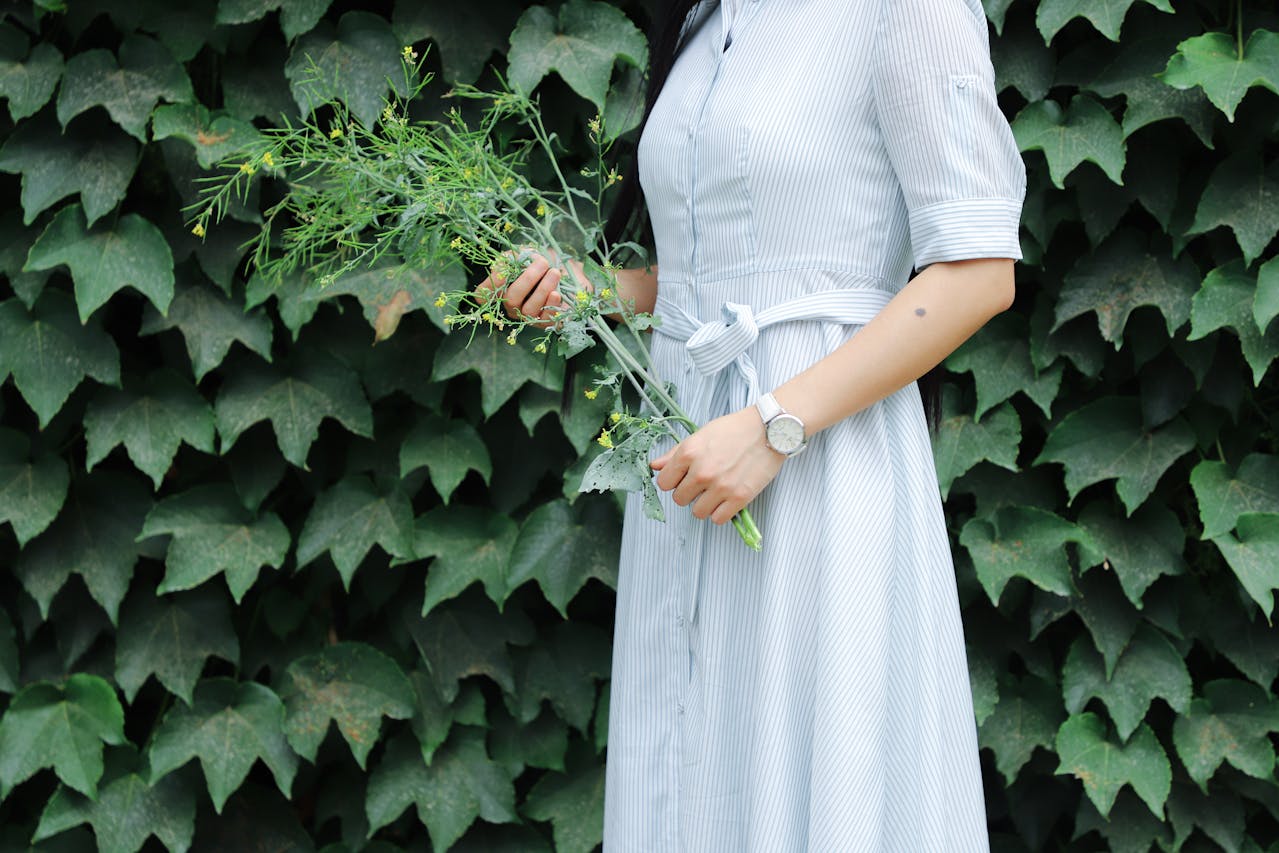 A wide view of a woman in a blue dress holding flowers and wearing a white watch.