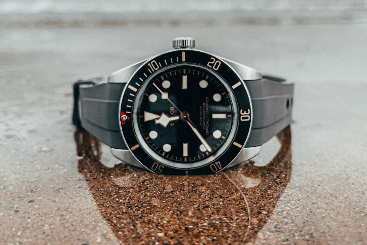 A close-up of a sporty TUDOR watch displayed on its side atop a slick and reflective granite surface.