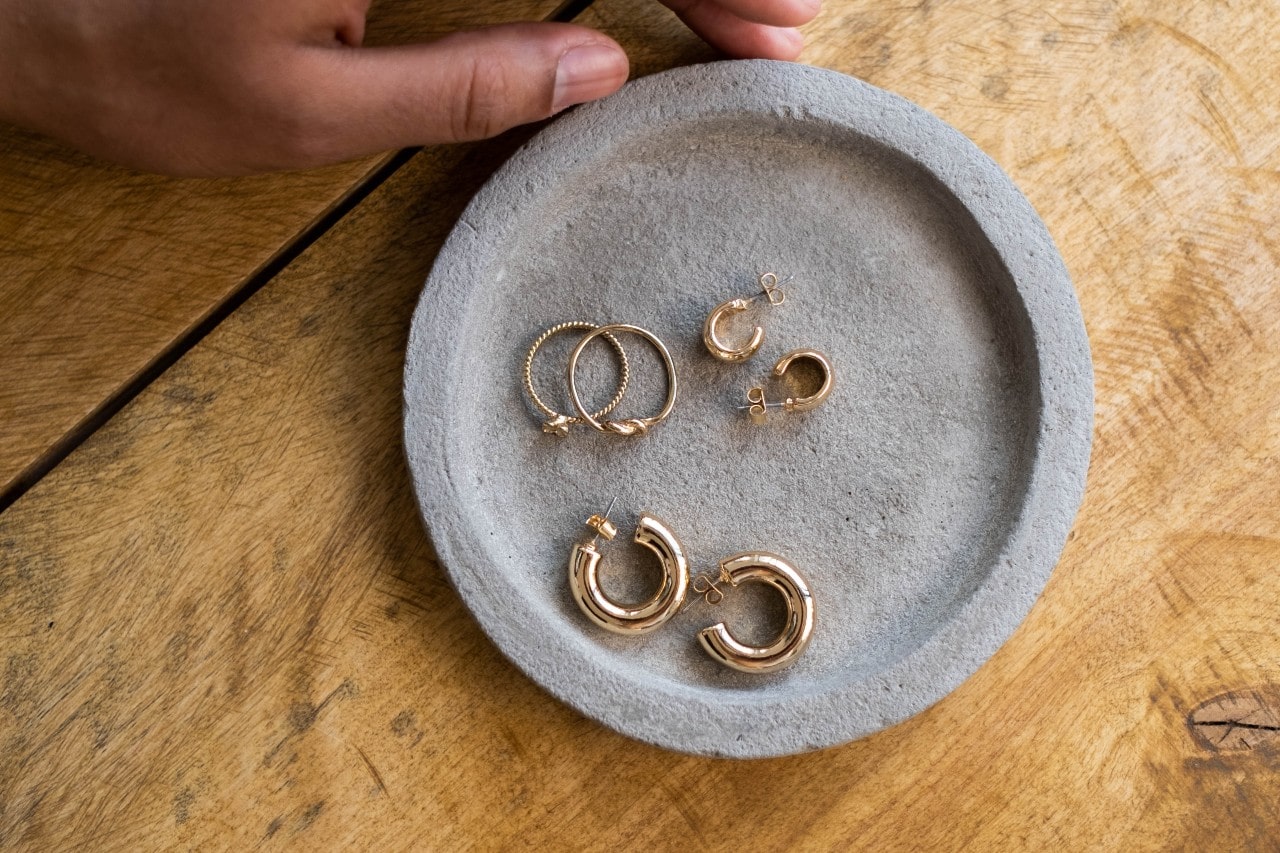 A gray dish on a wooden surface holding several pairs of gold hoop earrings in different sizes.