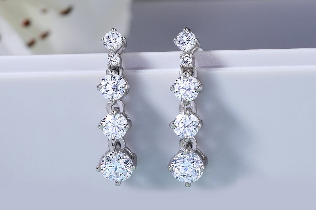 A pair of silver drop earrings set with multiple round sparkling diamonds.