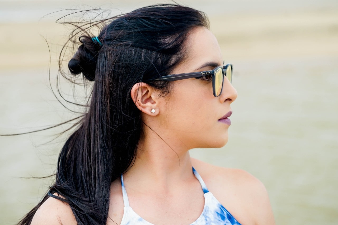 A close up of a woman with black hair and glasses, showcasing round diamond stud earrings.