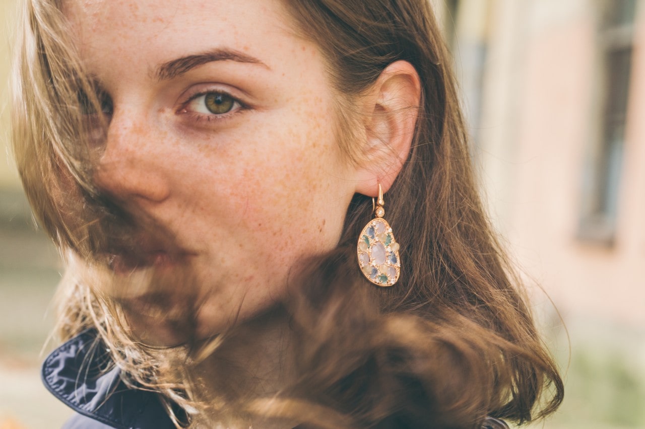 A woman looks over her shoulder as the wind blows, showing her gemstone drop earrings.
