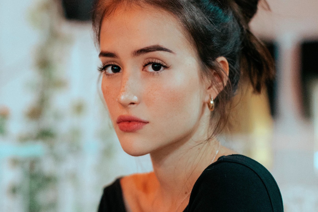 A woman with freckles looks at the camera, wearing gold huggies earrings.