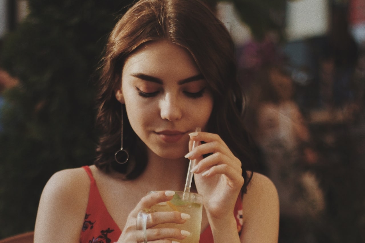 A woman sipping a limeade in a restaurant wears gold drop earrings.