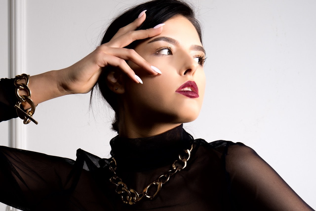 A woman in a black mesh top wears yellow gold chunky chain jewelry. A woman in a black mesh top wears yellow gold chunky chain jewelry.
