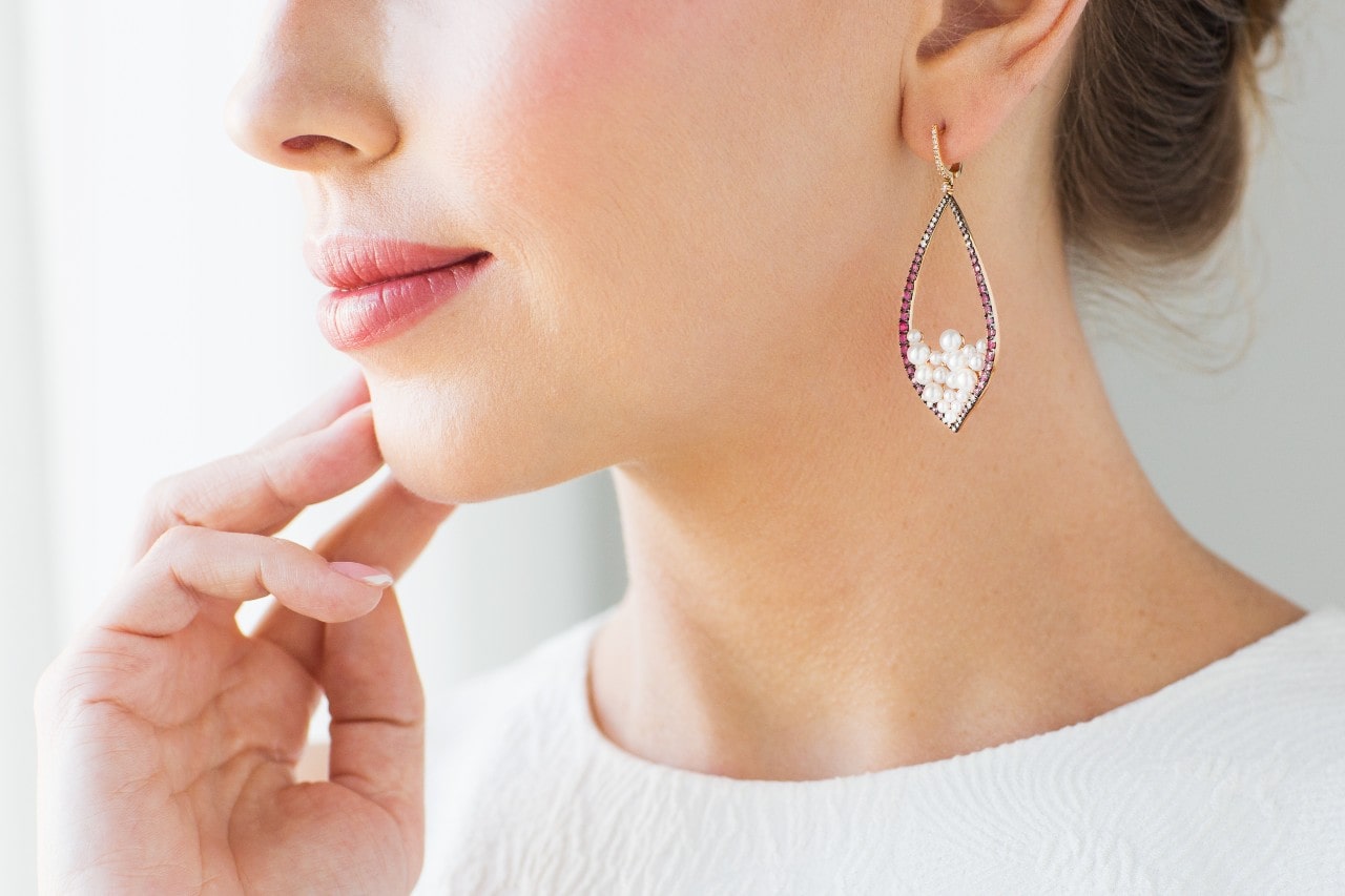 A woman wearing white and gemstone drop earrings looks outside.