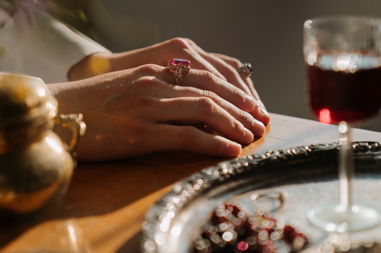 A woman at a dinner with wine rests her hands on the table, showing her two cocktail rings. A woman at a dinner with wine rests her hands on the table, showing her two cocktail rings.