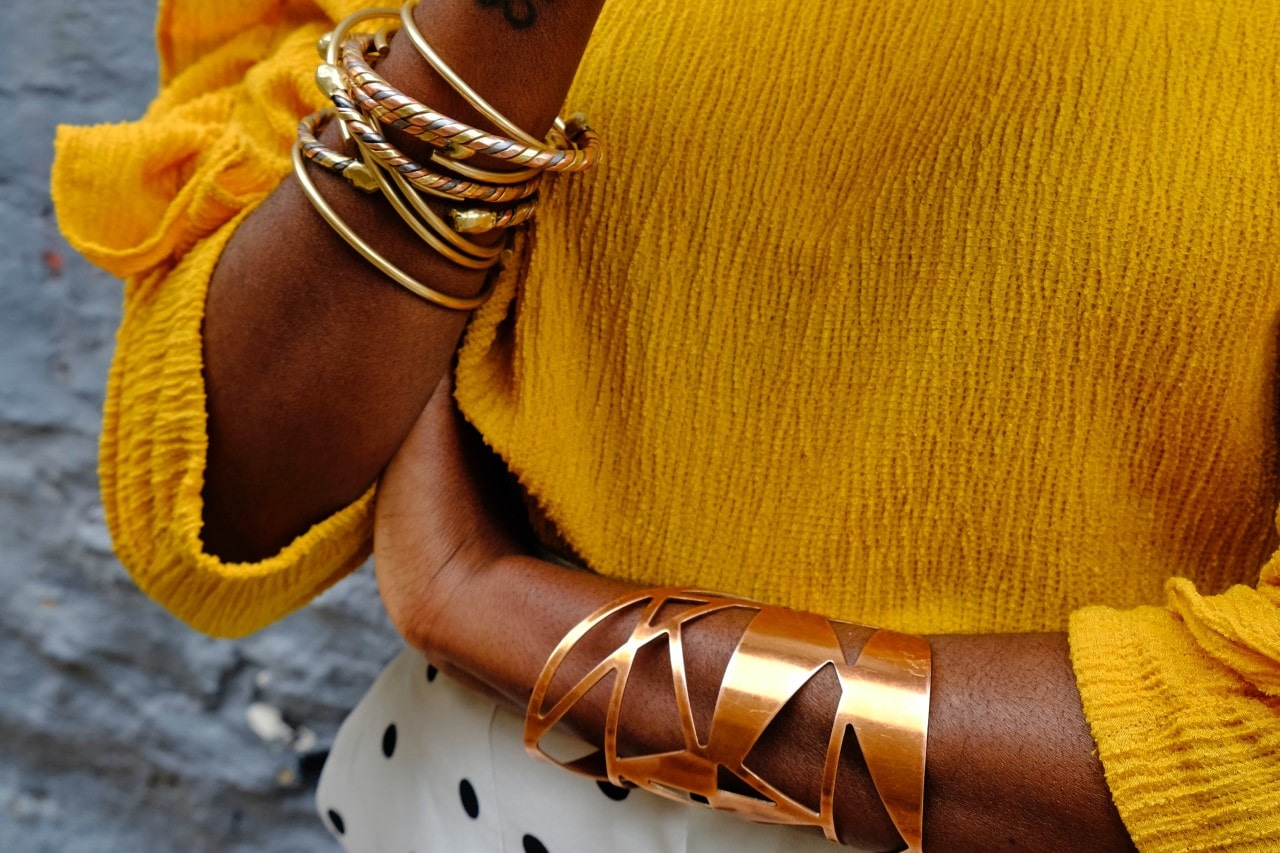A woman in a yellow blouse wears multiple gold bangles.