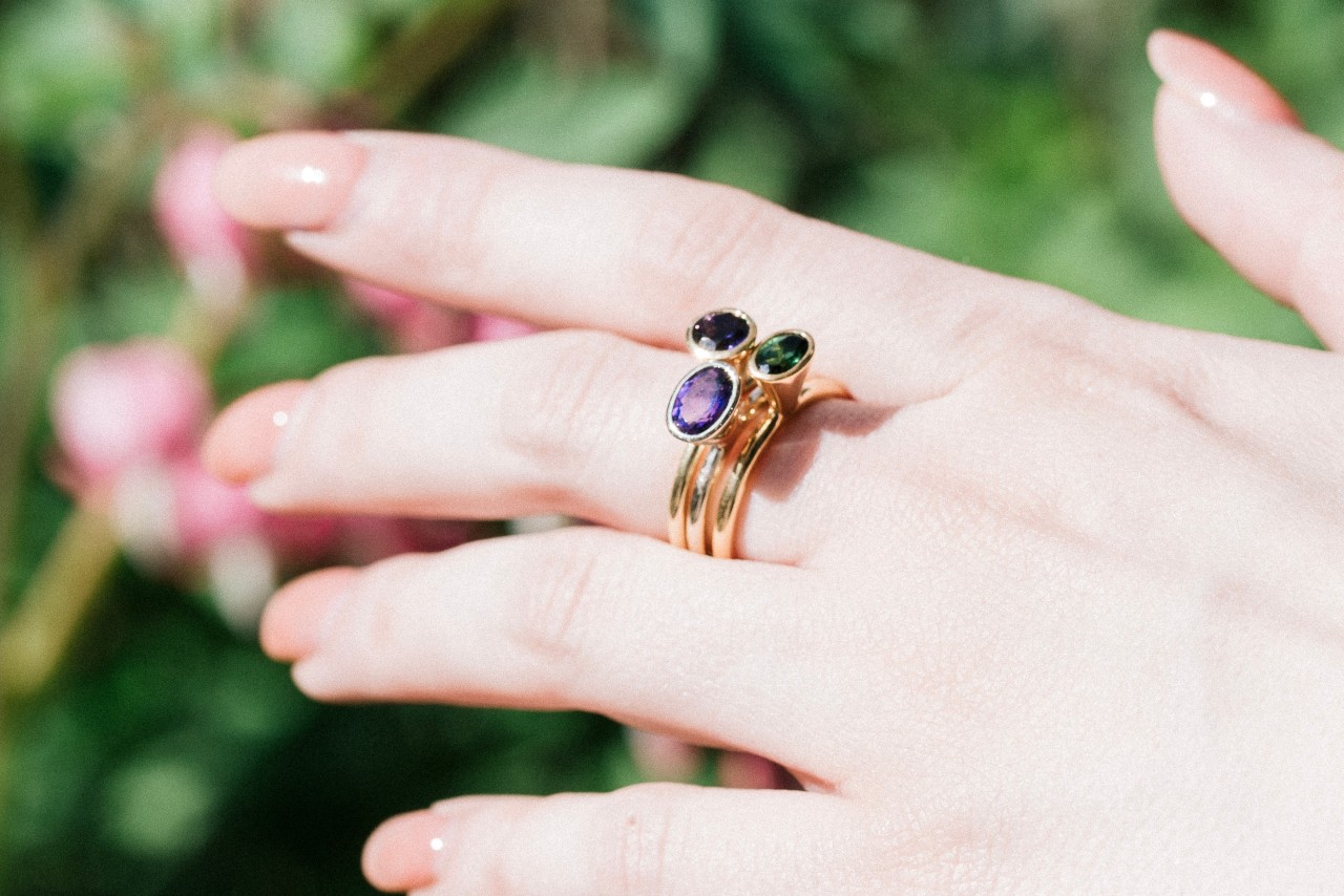 an extended hand wearing three yellow gold gemstone rings stacked on one finger