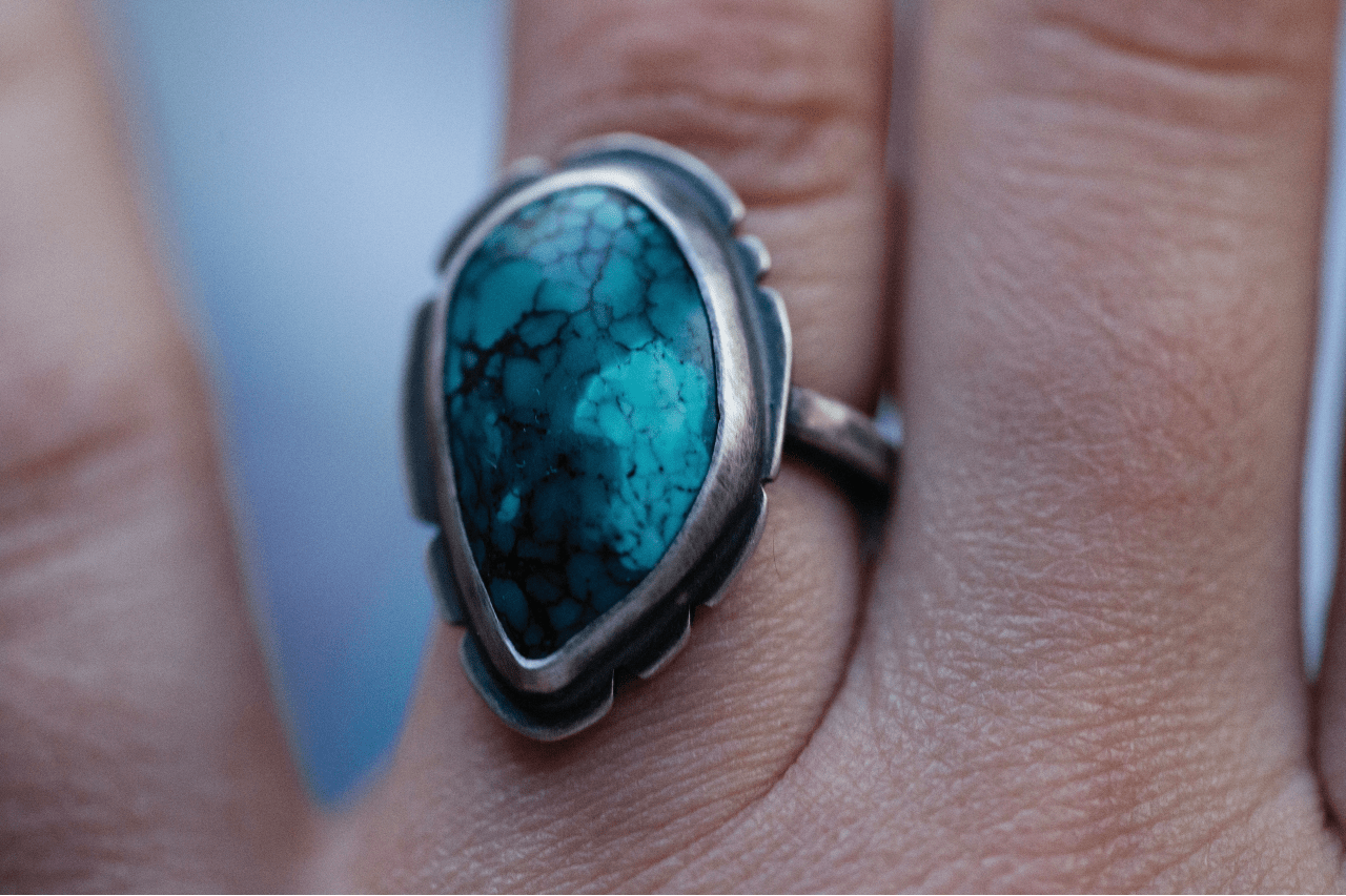 a white gold ring featuring a large turquoise stone on a person’s third finger